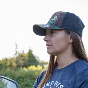 Woman wearing a Camo 'Hunt Fish Maniac Logo Trucker Hat in the field.