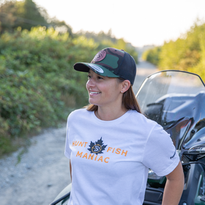 A woman wearing a White 'Hunt Fish Maniac' Classic Maple Leaf Crewneck Tee and camo baseball hat.